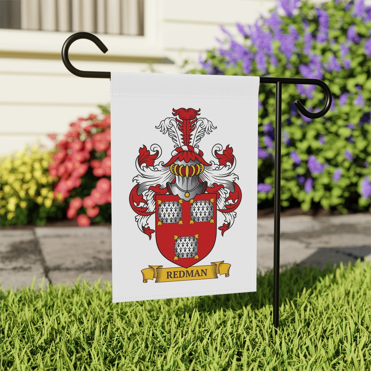 Personalized family crest flag with custom last name on a garden flagpole against a background of flowers and grass.
