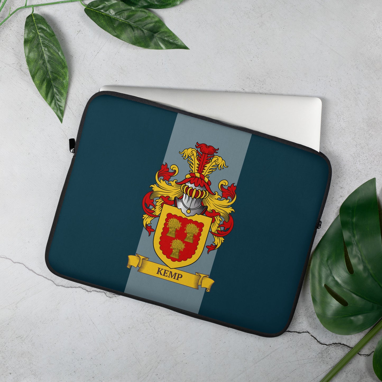 Teal Laptop sleeve with a coat of arms design on a light gray surface with green leaves.