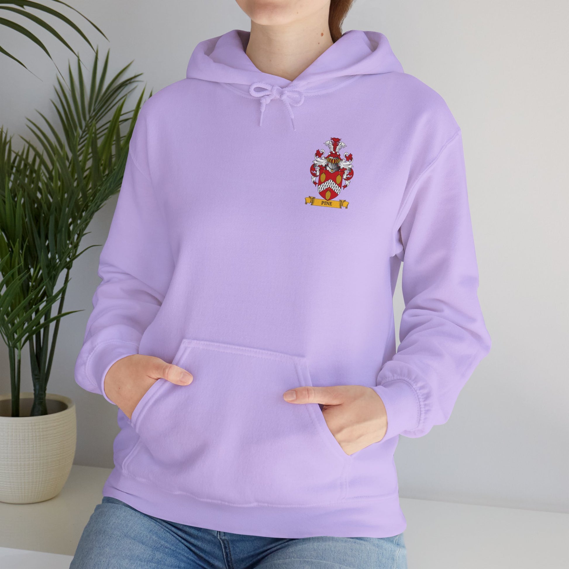 Woman wearing a lavender hoodie with a personalized family crest print, standing indoors next to a plant.