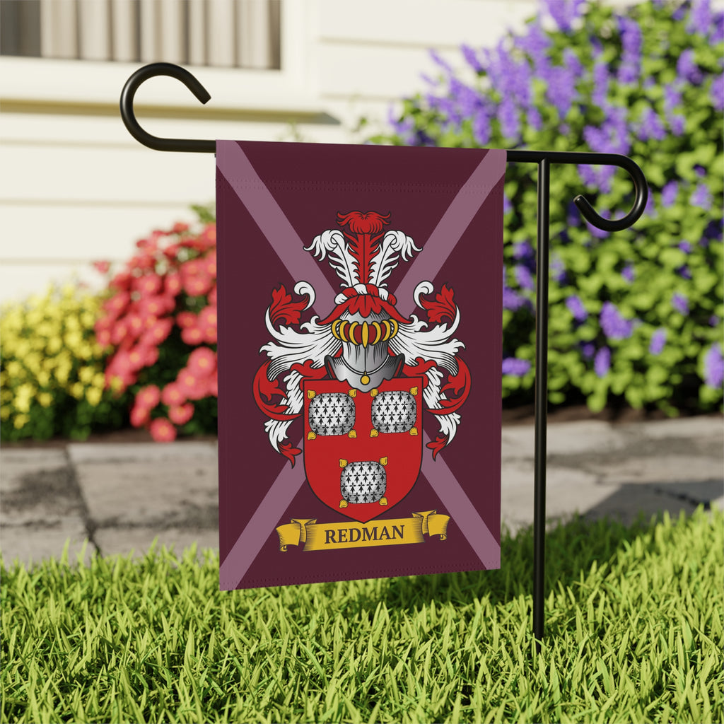 Garden flag with a customized coat of arms design on a maroon background, featuring the person's last name, against a garden backdrop with flowers and grass.
