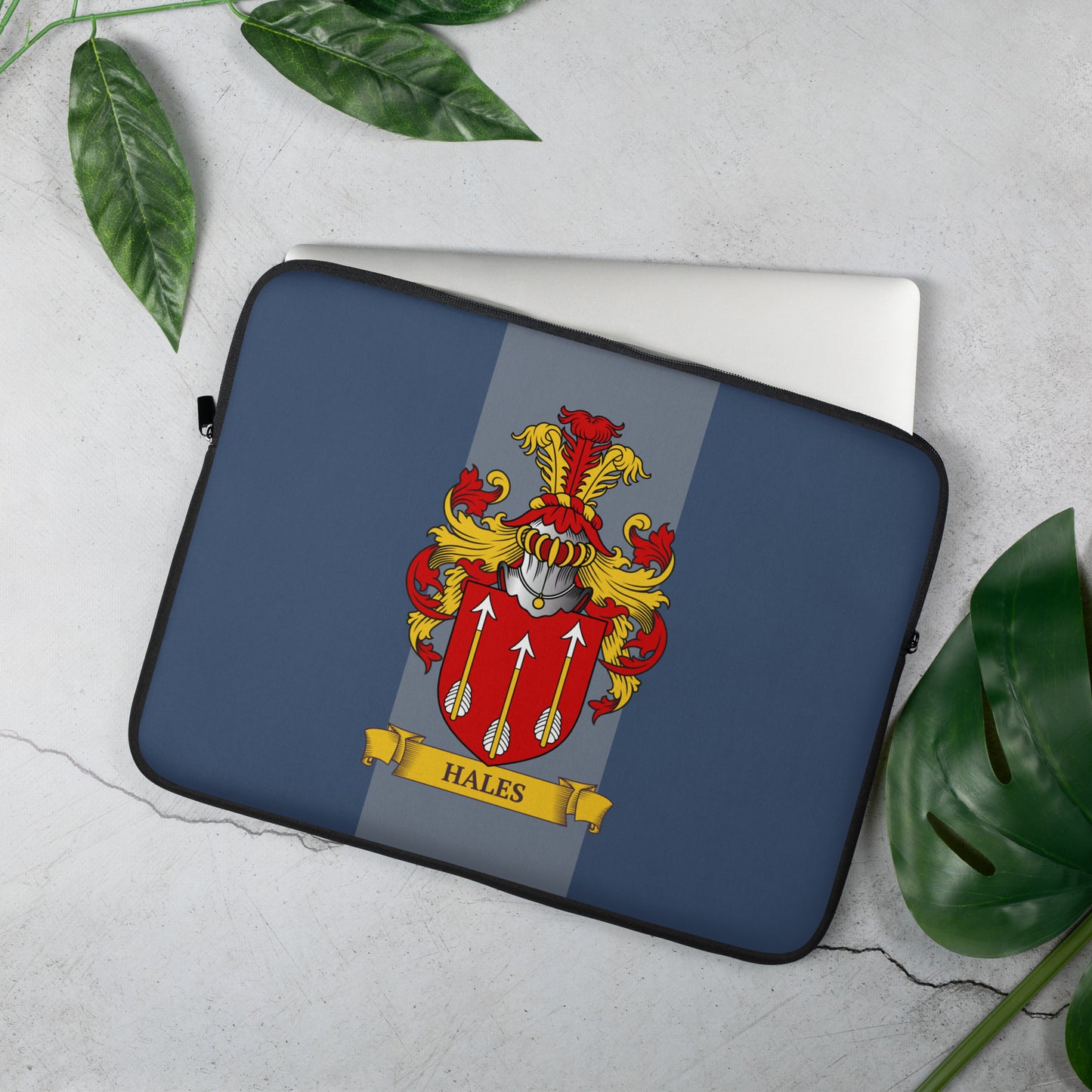 Laptop sleeve with a family crest design on a light gray surface with green leaves.