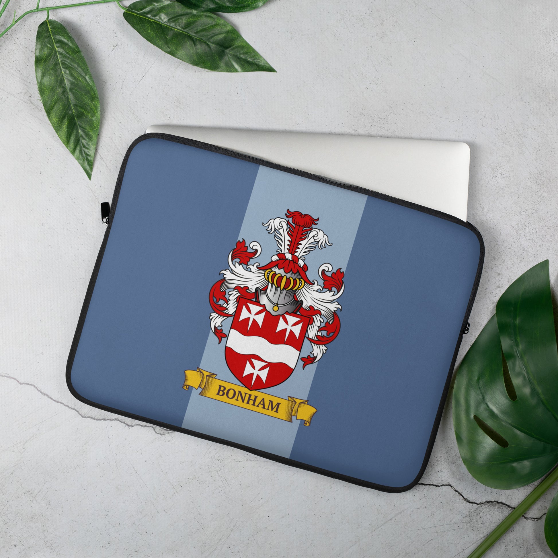 Blue Laptop sleeve with a coat of arms design on a light gray surface with green leaves.