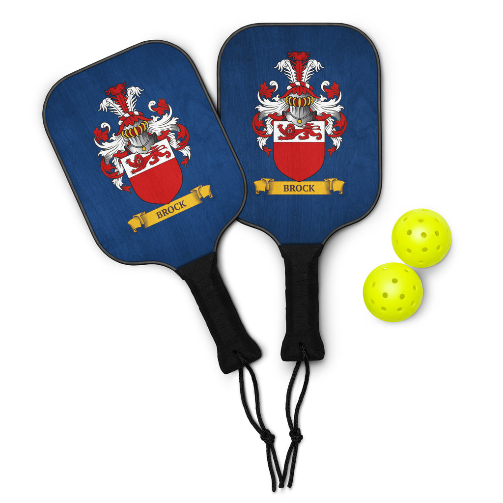Two pickleball paddles with a customized family crest design and accompanied by two yellow pickleballs on a white background.